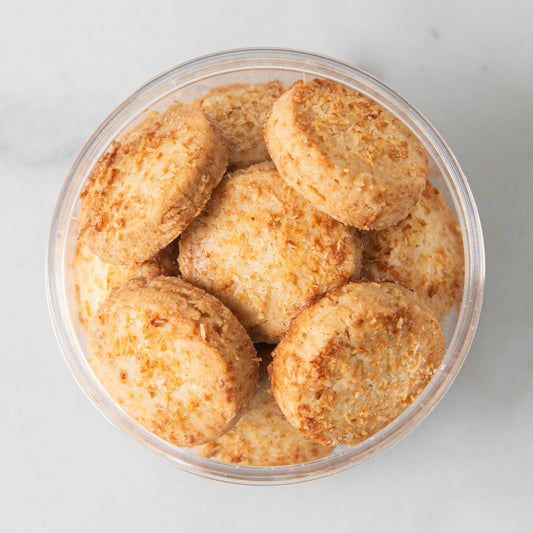 A top-down view of several round, golden-brown cookies or biscuits piled in a clear plastic container on a light gray marble surface.