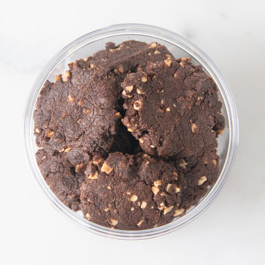 Chocolate chip cookies in a clear round plastic container, photographed from a top-down view on a light neutral background.