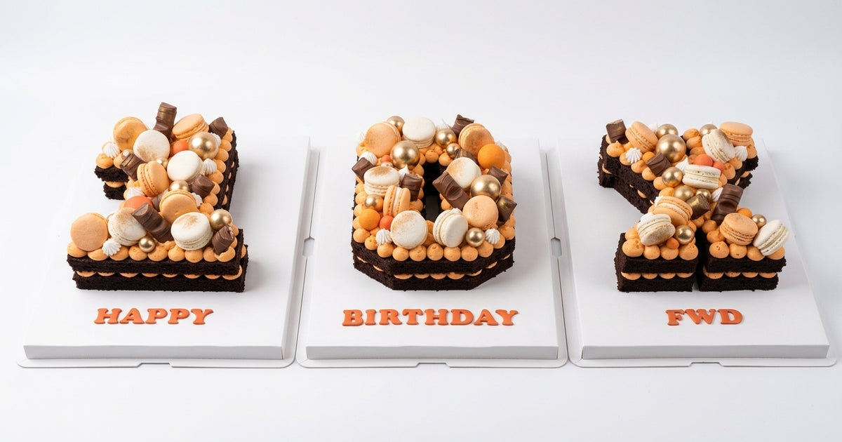Three custom chocolate and macaron number cakes displayed side-by-side on white stands against a clean white background. The left cake is shaped like the number 8 and is decorated with orange and beige macarons and chocolate, with 'HAPPY' written in orange at the base.
